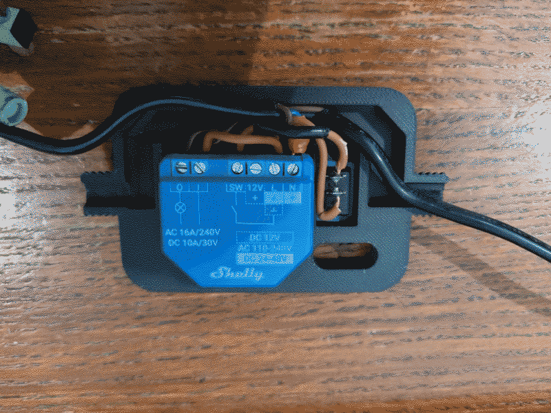 image of shelly device with mains power cable pluged in. The device is enclosed in a black 3d printed case.